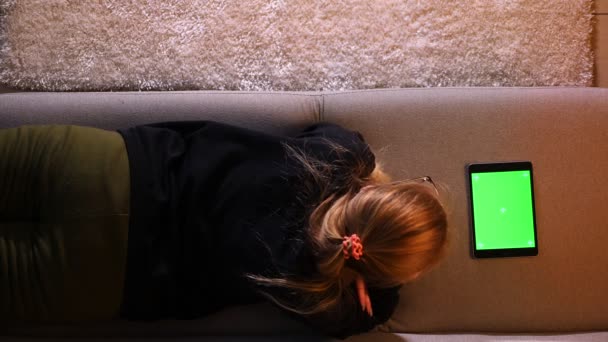 特写上背部拍摄漂亮的女孩使用平板电脑与绿色色度键屏幕，而躺在舒适的公寓室内的桌子上 — 图库视频影像