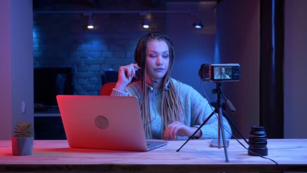Primer plano de la joven atractiva blogger con rastas en auriculares jugando videojuegos con el fondo de neón en el interior — Vídeo de stock