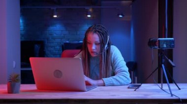 Kulaklık dreadlocks ile genç çekici kadın blogger Closeup ateş dizüstü bilgisayarda video oyunları oynarken ve kapalı neon arka plan ile başarısız