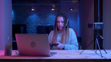 Kulaklık dreadlocks ile genç çekici kadın blogger Closeup ateş dizüstü bilgisayarda video oyunları oynarken ve neon arka plan kapalı üzgün olma başarısız