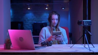 Kulaklık dreadlocks ile genç çekici kadın blogger Closeup ateş kapalı neon arka plan ile tablet kullanarak video oyunları hakkında konuşurken canlı akışı