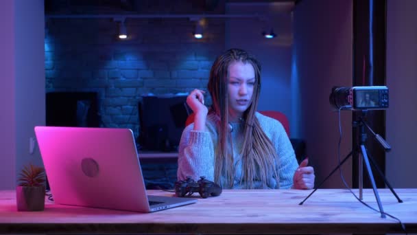 헤드폰에 공포를 가진 젊은 매력적인 여성 블로거의 클로즈업 촬영 은 실내 네온 배경과 노트북을 사용하여 비디오 게임에 대해 라이브 이야기 스트리밍 — 비디오