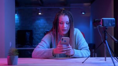 Neon arka plan kapalı canlı akan telefonda dreadlocks mesajlaşma ile genç çekici kadın blogger Closeup ateş
