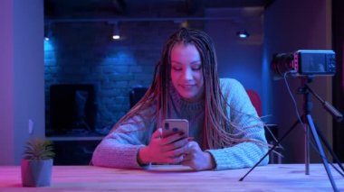 Dreadlocks telefonda mesajlaşma ile genç çekici kadın blogger Closeup ateş mutlu neon arka plan kapalı canlı akışı gülümseyerek