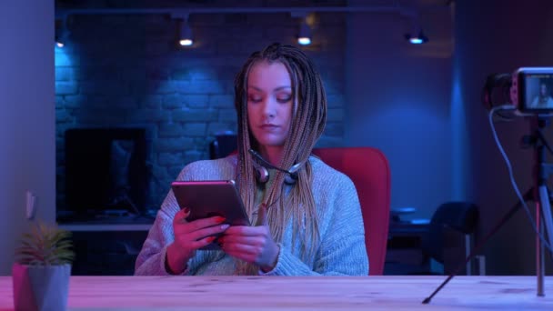 Gros plan shoot of young attractive female blogger in headphones streaming live using the tablet and showing green chroma screen to the camera with the neon background inside — Video