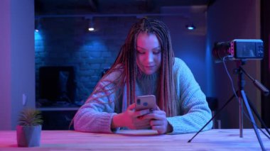 Telefonda dreadlocks mesajlaşma ile genç çekici kadın blogger Closeup ateş neon arka plan kapalı canlı akışı neşeyle gülümseyerek