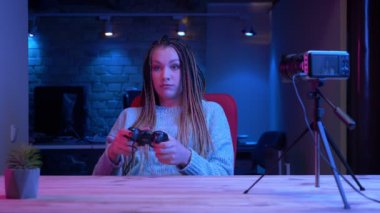 Dreadlocks oyun konsolu kapalı neon arka plan ile canlı akışı kullanarak video oyunları oynarken genç çekici kadın blogger Closeup ateş