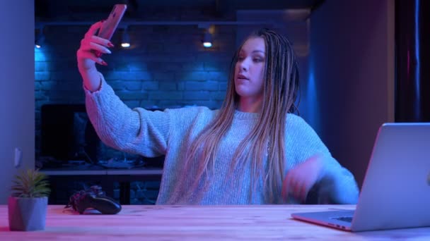 Zbliżenie strzelać młodych atrakcyjnych kobiet blogger z dredy streaming na żywo w telefonie za pomocą laptopa z Neon tła w pomieszczeniu — Wideo stockowe