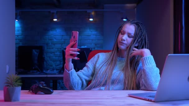 Nahaufnahme einer jungen attraktiven Bloggerin mit Dreadlocks, die live auf das Handy mit dem Neon-Hintergrund drinnen streamt — Stockvideo