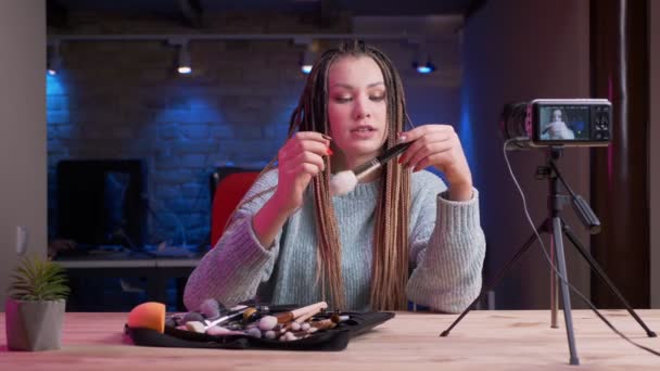 Sesión de primer plano de una joven y atractiva bloguera con rastas en directo y discutiendo los productos de belleza con el fondo de neón en el interior — Vídeos de Stock