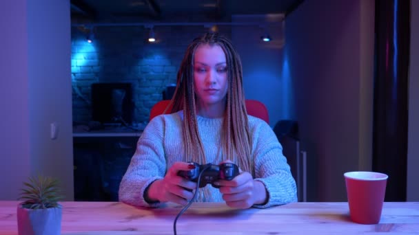 Sesión de primer plano de una joven y atractiva blogger con rastas jugando videojuegos usando la consola de juegos en streaming con el fondo de neón en el interior — Vídeos de Stock