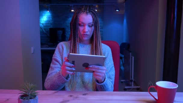 タブレットでビデオゲームをプレイドレッドロックを持つ若い魅力的な女性ブロガーのクローズアップ撮影は、屋内でネオンの背景とライブストリーミング幸せであること — ストック動画