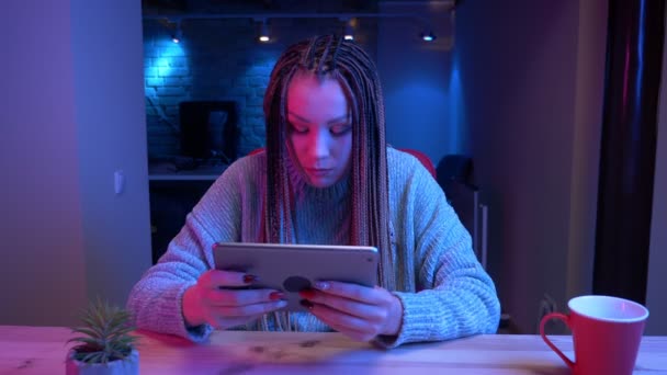 Tiro de close-up de jovem blogueiro feminino atraente com dreadlocks jogar jogos de vídeono tablet perder e ser frustrado streaming ao vivo com o fundo de néon dentro de casa — Vídeo de Stock