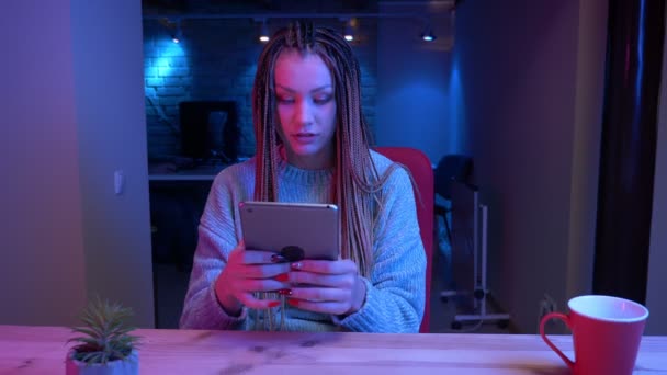 Sesión de primer plano de una joven bloguera atractiva con rastas jugando videojuegos en la tierra de la tableta mostrando la pantalla de croma verde en vivo con el fondo de neón en el interior — Vídeo de stock