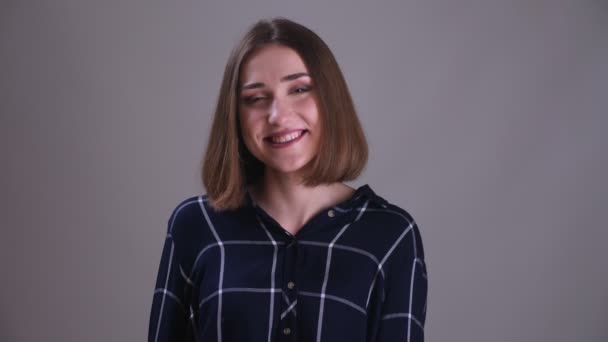 Närbild shoot av unga ganska korthårig kvinna tittar på kamera och leende med bakgrund isolerade på grått — Stockvideo