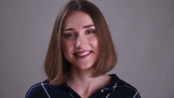 Närbild shoot av unga ganska korthårig kvinnlig ansikte tittar på kamera med söta leende ansiktsuttryck med bakgrund isolerade på grått — Stockvideo