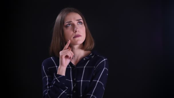 Gros plan pousse de jeune jolie femelle aux cheveux courts être réfléchi et avoir une idée en regardant la caméra et en souriant avec un fond isolé sur noir — Video