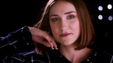 Utangaçlık ile gülümseyen ve arka planda bokeh ışıkları ile kamera önünde poz genç sevimli kısa saçlı kadın Closeup ateş