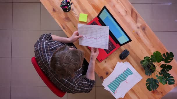 Primo piano top shot di giovane uomo d'affari caucasico digitando sul computer portatile sulla scrivania e studiando grafici in ufficio al chiuso — Video Stock