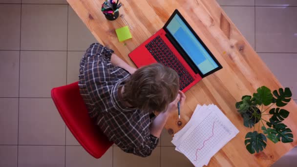 Primer plano sesión superior de joven hombre de negocios caucásico escribiendo en el ordenador portátil en el escritorio y tomando notas en la oficina en el interior — Vídeos de Stock