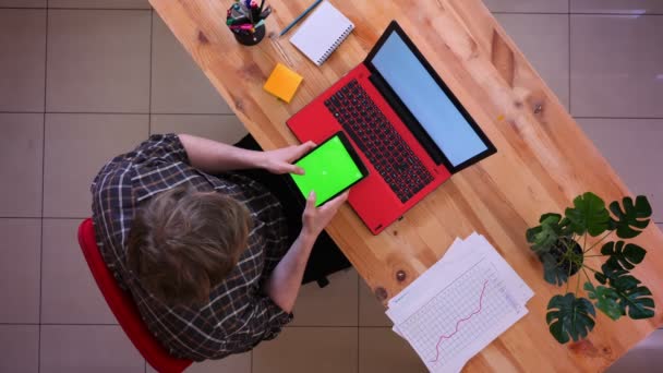 Close-up top shoot van jonge Kaukasische zakenman met behulp van de Tablet met groene Chroma scherm zittend voor de laptop op het Bureau in het kantoor binnenshuis — Stockvideo