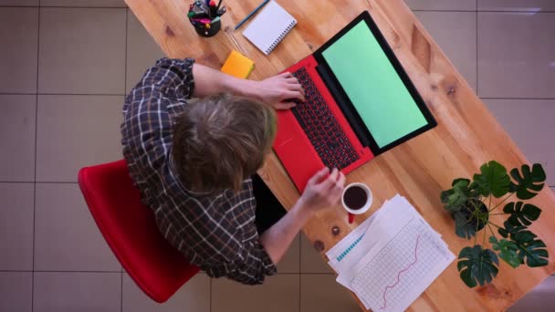 Primer plano superior de la sesión de jóvenes caucásicos hombre de negocios escribiendo en el portátil y beber café en la oficina en el interior — Vídeo de stock