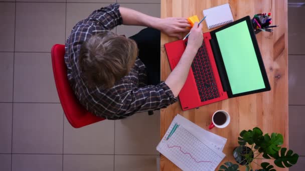 Primer plano sesión superior de joven hombre de negocios caucásico trabajando en el ordenador portátil con pantalla verde y haciendo un recordatorio de una cita con el café en la oficina en el interior — Vídeos de Stock