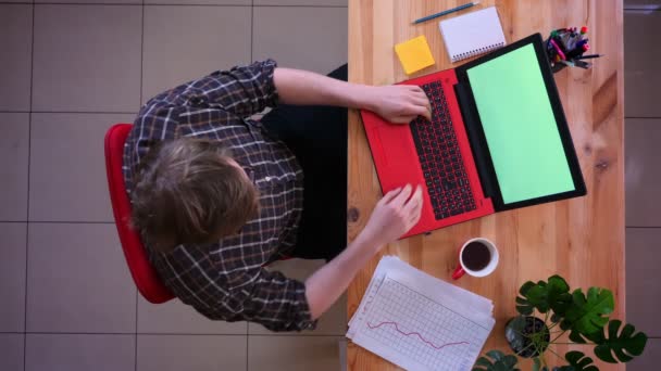 Yeşil ekranlı dizüstü bilgisayar üzerinde çalışan ve ofis kapalı kahve ile grafikleri analiz genç kafkas işadamı closeup üst çekim — Stok video