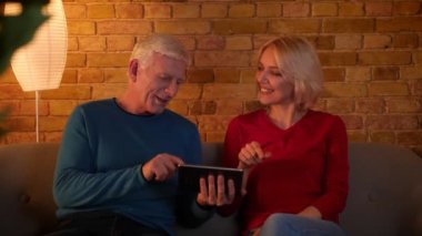 Tablet kullanarak üst düzey mutlu çift Closeup ateş ve rahat bir dairede kanepede oturan mutlu gülümseyerek