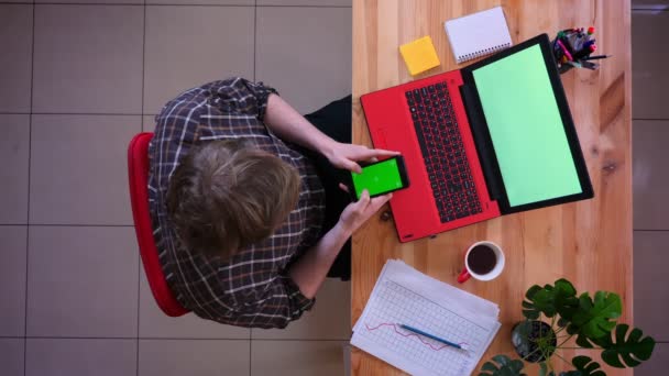 Primo piano riprese top di giovane uomo d'affari caucasico utilizzando il telefono con schermo verde di fronte al computer portatile con caffè in ufficio al chiuso — Video Stock