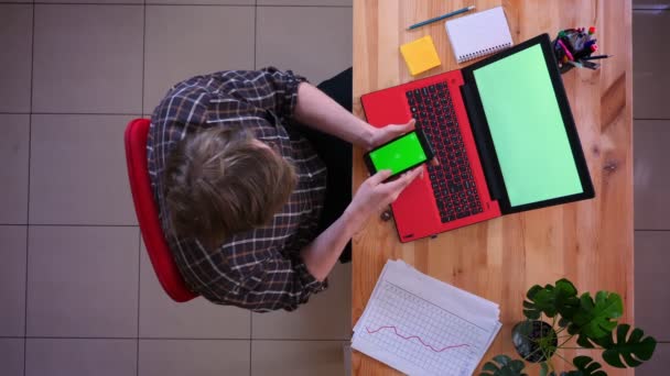 Close-up top shoot van jonge Kaukasische zakenman met een gesprek op de telefoon met groene Chroma scherm voor de laptop in het kantoor binnenshuis — Stockvideo