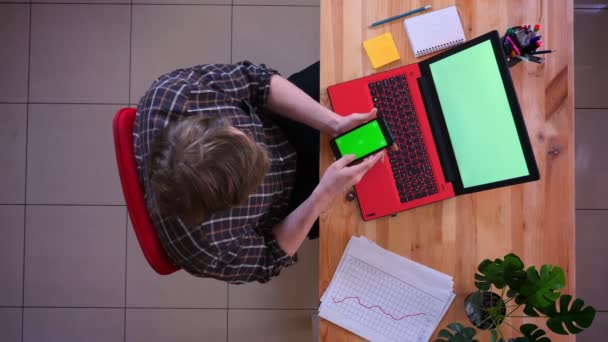 Primo piano top shot di giovane uomo d'affari caucasico che ha una conversazione al telefono con schermo cromato verde di fronte al computer portatile in ufficio al chiuso — Video Stock