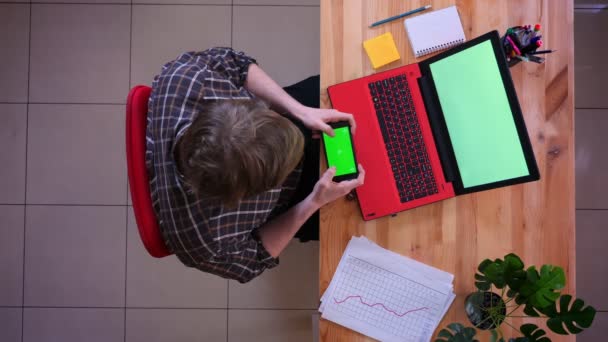 Primo piano top shoot di giovane uomo d'affari caucasico messaggiare al telefono con schermo cromato verde di fronte al computer portatile in ufficio al chiuso — Video Stock