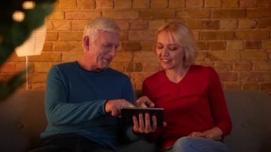 Rahat bir dairede kapalı kanepede oturan tablet üzerinde sosyal medya sörf üst düzey mutlu çift Closeup ateş