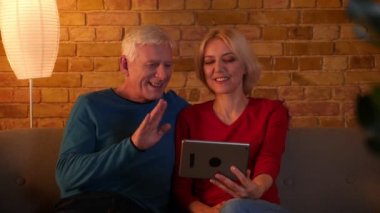 Rahat bir dairede kanepede otururken neşeyle konuşurken tablet üzerinde bir video arama olan üst düzey mutlu çift Closeup ateş