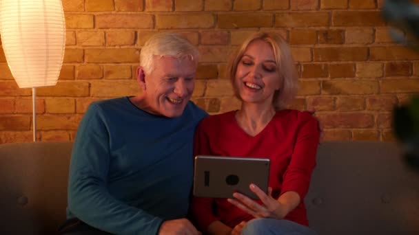 Closeup shoot of senior happy couple having a video call on the tablet sitting on the couch indoors in a cozy apartment — Stock Video