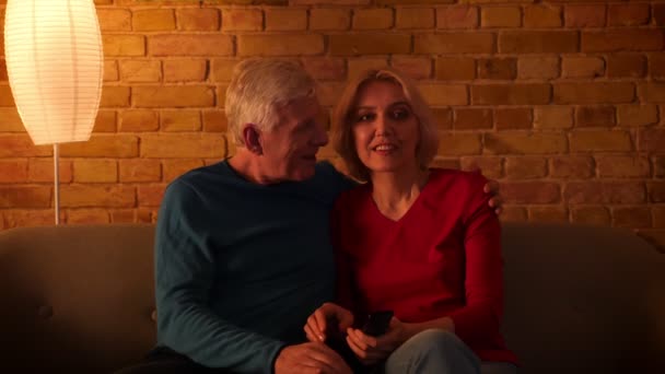 Närbild shoot av Senior Happy Couple tittar på TV leende glatt sitter på soffan inomhus i en mysig lägenhet — Stockvideo