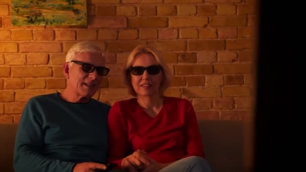 Closeup focení starších šťastných pár sleduje 3D film v TV, který sedí na pohovce doma v útulném bytě