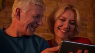 Rahat bir dairede kanepede oturan tablet kullanarak yaşlı mutlu çift Closeup ateş