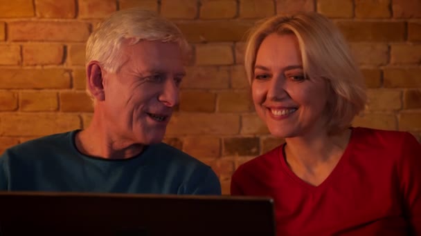 Primer plano sesión de ancianos feliz pareja viendo una película en el portátil sentado en el sofá en un acogedor apartamento — Vídeos de Stock