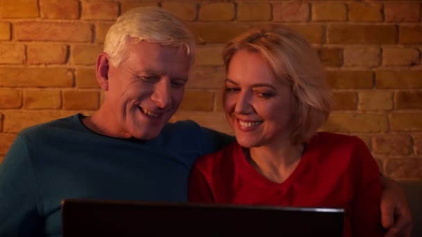 Rahat bir dairede kanepede oturan sevinçle gülümseyen dizüstü bilgisayar kullanarak yaşlı mutlu çift Closeup ateş — Stok video
