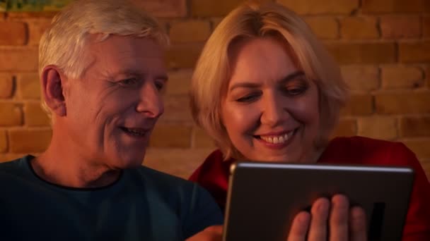 Primer plano de la sesión de ancianos feliz pareja teniendo una videollamada en la tableta sonriendo alegremente sentado en el sofá interior en un acogedor apartamento — Vídeos de Stock