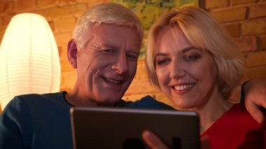 Rahat bir dairede birlikte dinlenme kanepede oturan tablet üzerinde yaşlı mutlu çift tarama web Closeup ateş