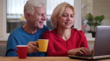 Masanın üzerinde dizüstü bilgisayarda üst düzey mutlu çift ağ closeup ateş ve rahat bir dairede kapalı kahve içme