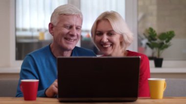 Rahat bir dairede kapalı masada çay ile bardak ile dizüstü bilgisayarda bir video arama olan yaşlı mutlu çift Closeup ateş