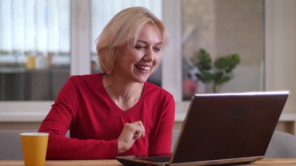 Tiro de close-up de mulher caucasiana envelhecida ter uma chamada de vídeo no laptop sorrindo alegremente dentro de casa em um apartamento acolhedor — Vídeo de Stock