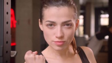 Genç çekici atlet kadın kamera bakarak ve salonda spor salonunda güçlü bir yumruk gösteren Closeup ateş