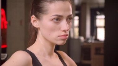 Bir at kuyruğu ile genç çekici atlet kadın Closeup ateş kamera bakarak motive olmak ve kapalı spor salonunda egzersiz için hazırlanıyor