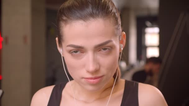 Primer plano de la joven atleta atractiva mujer poniendo en sus vibraciones mirando a la cámara en el gimnasio en el interior — Vídeo de stock