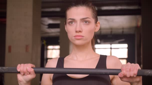 Sesión de primer plano de la joven atleta atractiva mujer caminando y preparándose para levantar pesas mirando a la cámara en el gimnasio en el interior — Vídeos de Stock